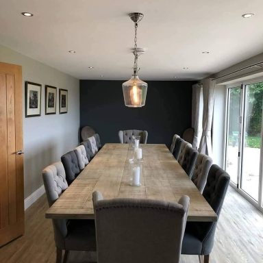 A spacious dining room with a long table, grey chairs, and natural light.