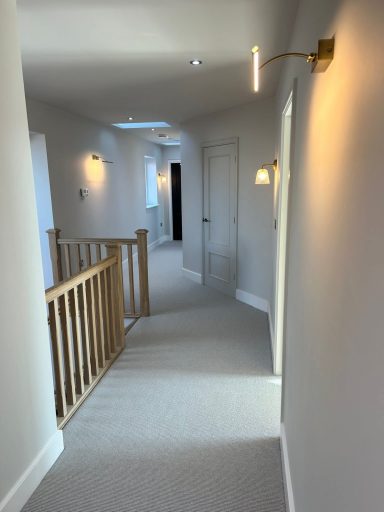 Bright corridor with a wooden balustrade, lighting, and a door at the end.
